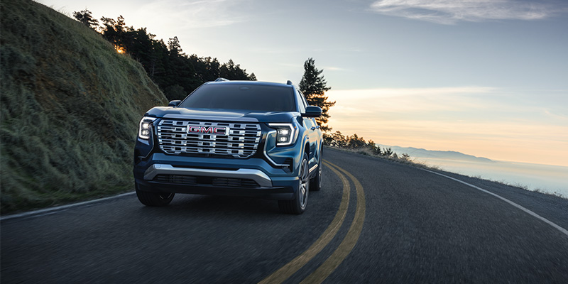 A blue GMC SUV driving on a scenic mountain road.
