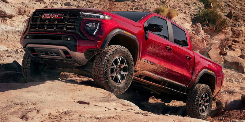 A red GMC pickup truck driving over large, rocky terrain.
